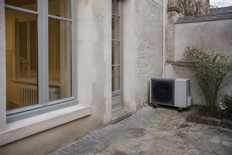 Cour arrière d'une maison de bourg avec une unité extérieure de pompe à chaleur air-eau dans un coin